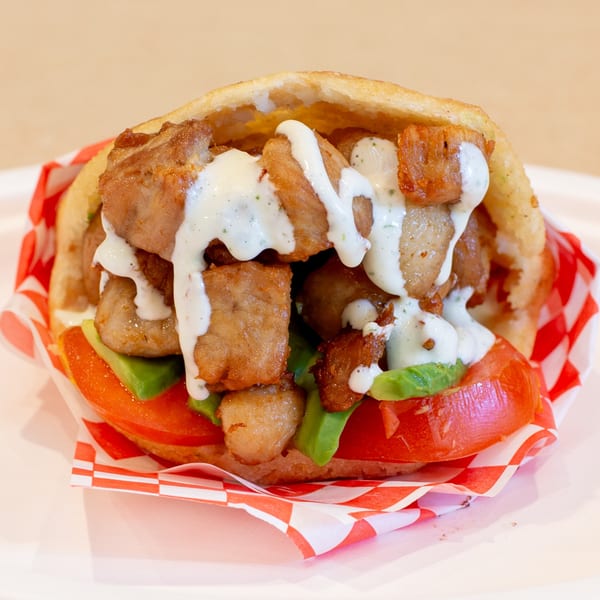 Venezuelan Chamo Cuisine's Arepa with fried pork, avocado, tomato, and white sauce in a red checkered wrapper.