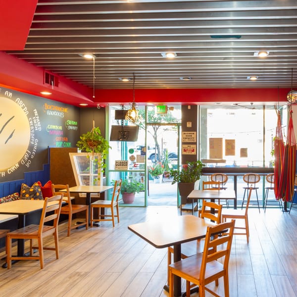 Venezuelan Chamo Cuisine's vibrant dining area with wooden tables, benches, and a colorful hammock by the window.
