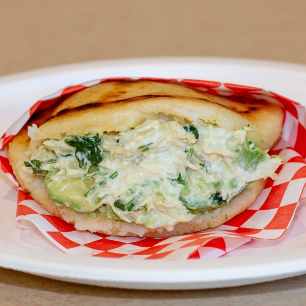 Venezuelan Reina Pepiada Arepa, a cornmeal patty filled with chicken salad and avocado, on a white plate.