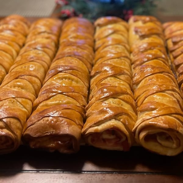 Rows of golden-brown, braided Venezuelan pastries, likely cachitos, on a dark surface.