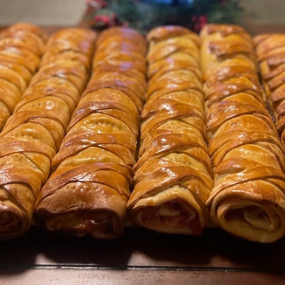 Rows of golden-brown, braided Venezuelan pastries, likely cachitos, on a dark surface.