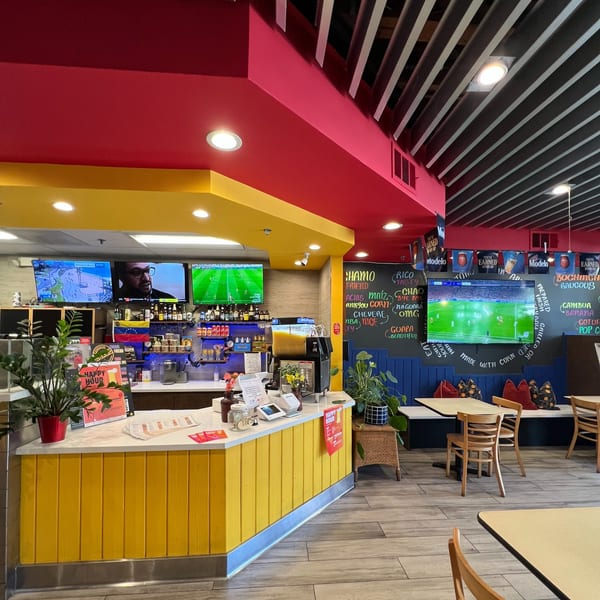 Colorful restaurant interior with yellow and red walls, multiple TVs, a bar, and dining tables.