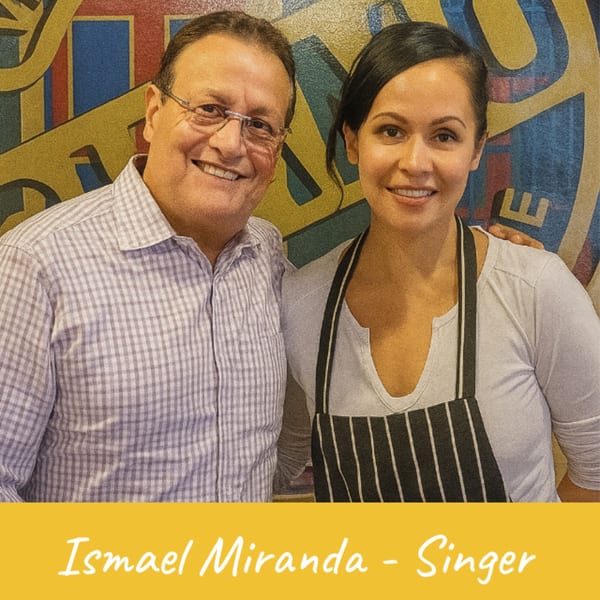 Venezuelan Chamo Cuisine owner and a woman in an apron smiling in front of a colorful mural.
