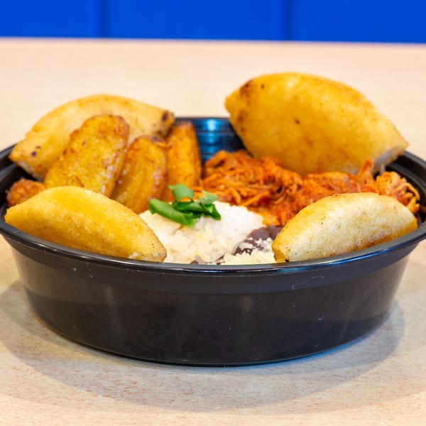 Venezuelan Chamo Cuisine meal with empanadas, plantains, shredded meat, rice, and beans in a black bowl.