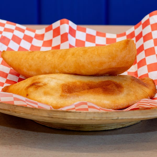 Two golden-fried Venezuelan empanadas in a wooden bowl lined with red and white checkered paper.